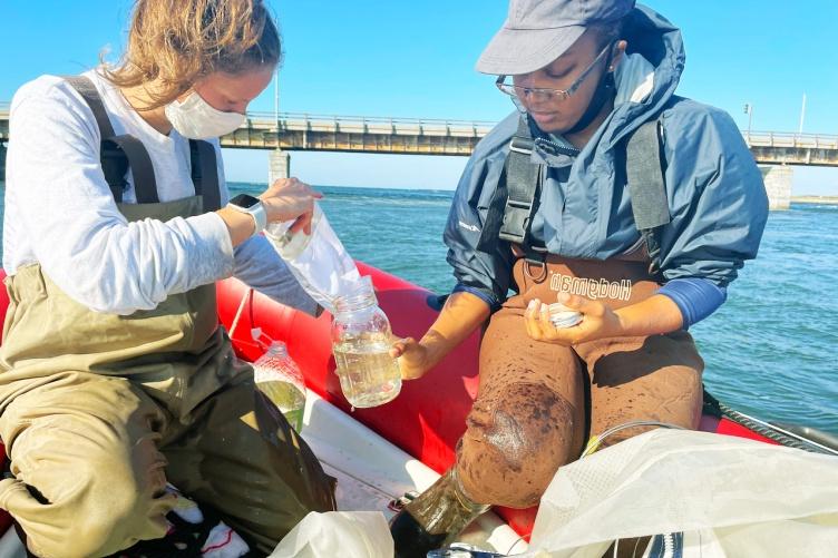 Two researchers sit on a boat looking through samples collecting from the estuary for microplastics.