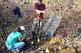 Two researchers (1 male standing, holding a shovel, 1女蹲在旁边整)在规定的烧伤地点工作种植盆栽红橡树.